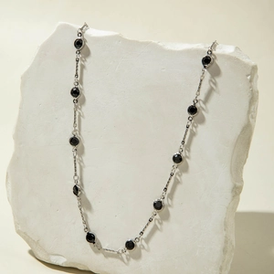 Detalle del collar de cadena plateada con gemas negras facetadas sobre piedra decor