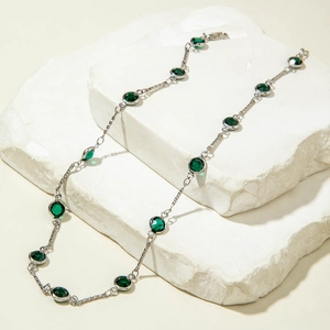 Detalle de collar de plata con pedrería verde sobre una superficie de piedra blanca