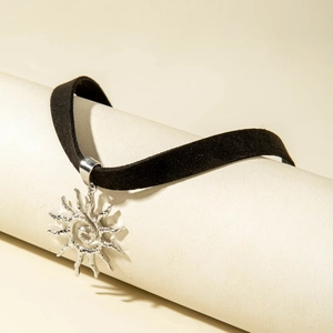 Detailopname van een zwarte fluwelen choker met een metallic zonvormige hanger in spiraal