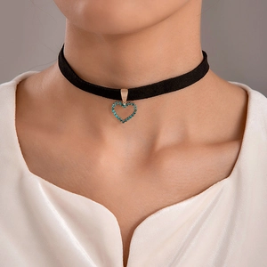 Detail van gothic zwarte fluwelen choker met roségouden hartvormige hanger en blauwe kristallen