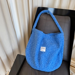 Detail of blue faux shearling tote bag featuring a minimalist white rectangular brand label