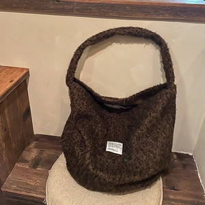 Detailed view of a brown plush tote bag with white woven label on a wooden bench