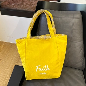 Dettaglio borsa shopper gialla con interno in peluche e stampa Faith su sedia grigia