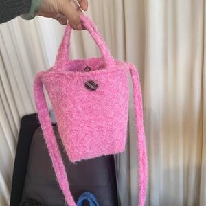 Détail d'un sac seau en peluche rose avec bouton à damier et fermeture magnétique