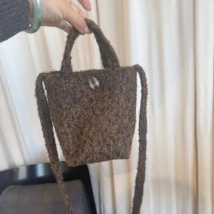 Détail d'un sac à main en polaire marron avec bouton à carreaux et bandoulière