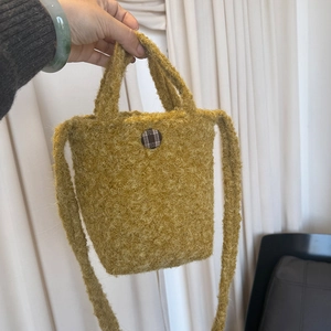 Détail du sac bandoulière en polaire jaune avec un bouton décoratif à carreaux bruns