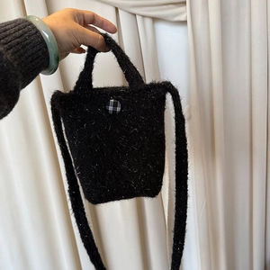 Détail d'un petit sac bandoulière en peluche noire avec un bouton à carreaux classique