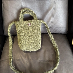 Détail du mini sac cabas en peluche verte avec bouton à carreaux sur une chaise en cuir