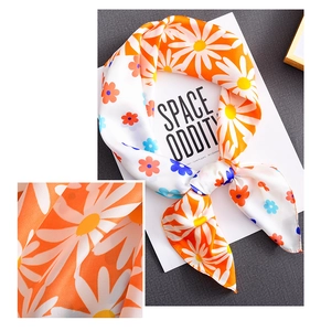 Detail of semi-transparent orange silk scarf with white daisy floral pattern and smooth texture