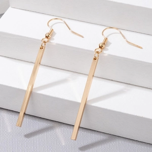 Close-up of golden geometric rectangular bar earrings on a minimalist white pedestal