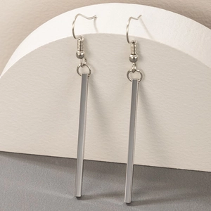 Close-up of geometric silver metal bar drop earrings hanging on a white display stand