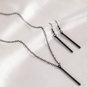 Minimalist black geometric necklace and earrings set displayed on white silk fabric