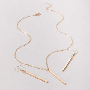 Detail of gold geometric bar necklace and drop earrings set on light grey background