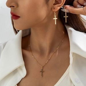 Close-up of a gold cross pendant necklace and matching drop earrings on a model