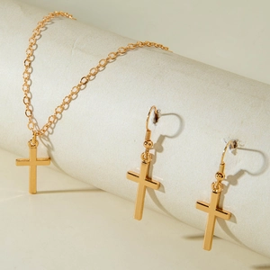 Detail view of a gold geometric cross jewelry set including necklace and drop earrings
