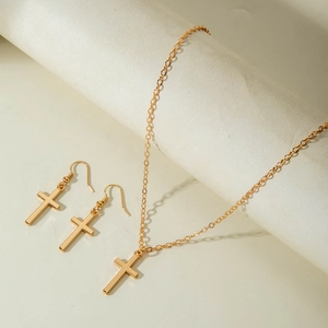 Golden cross jewelry set with necklace and drop earrings on a minimalist background