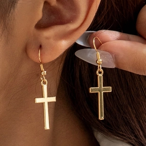 Close-up of elegant gold cross earrings on a model showing the polished drop hook design