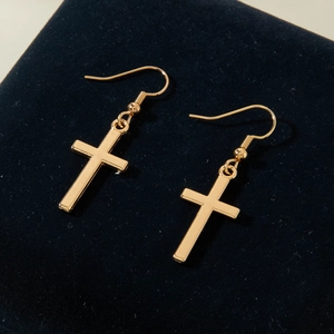 Close-up of golden cross earrings on blue velvet padding with secure fish hook design