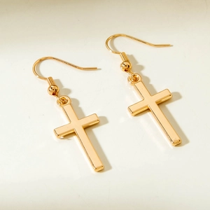 Detailed close-up of polished gold cross pendant earrings with minimalist metal ear hooks