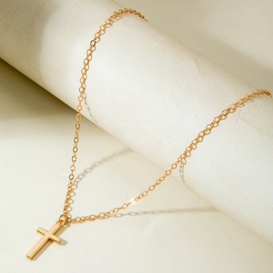 Close-up of minimalist golden cross pendant hanging on a white cylindrical stand