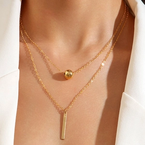 Detail of layered gold necklace with bead and vertical bar pendants on model