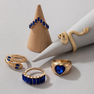 Dettaglio del set di 5 anelli dorati con pietre blu a cuore e motivi a serpente