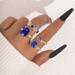 Dettaglio di un set di quattro anelli d'oro con pietre blu e design a corona sulle dita