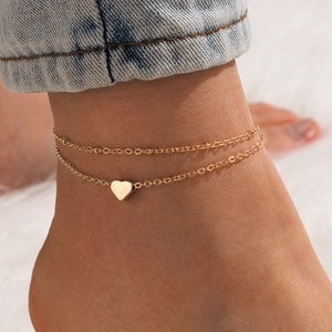 Close-up of gold double-layer anklet with heart pendant and delicate beads on ankle