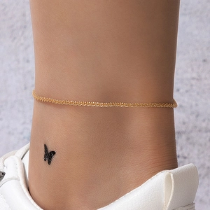 Close-up of golden wavy textured anklet chain on ankle with white sneakers