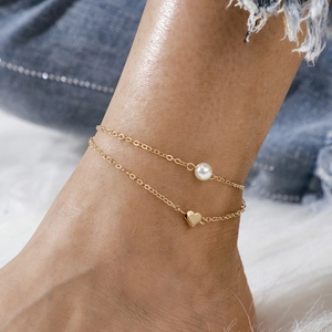Close-up of double-layer gold anklet with white pearl and heart pendant on ankle