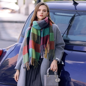 Thick colorful plaid scarf with long tassels worn with a grey wool coat in a street setting