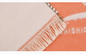 Close-up of knit fabric texture with tassel edge and woven text on winter neck scarf