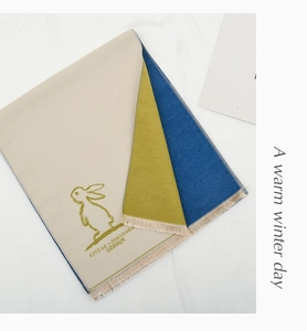 Detail of knit children shawl with rabbit print, brand lettering and tassel trim