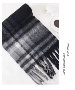 Close-up of black, grey and white plaid scarf with decorative tassels on a white surface