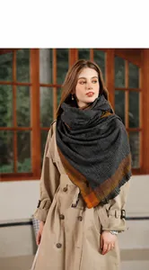 Détail d'une écharpe à carreaux avec bordure orange et franges sur un trench camel