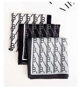 Close-up of monogram pattern silk scarves in black, white, and grey with contrast edges