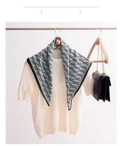 Close-up of silk square scarf with letter pattern draped over a white knit top with a bag