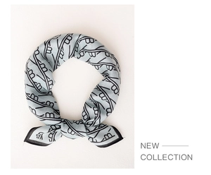 Detail of light blue silk square scarf with black abstract letter patterns and soft knots
