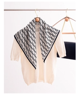 Detail of silk scarf with black monogram pattern on cream knitwear and wooden hanger