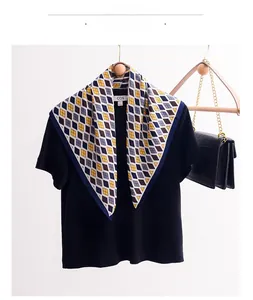 Detailed close-up of argyle plaid silk scarf tied on black shirt with luxury handbag