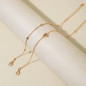 Detail of layered gold ankle chains featuring a polished heart pendant and tiny gold beads