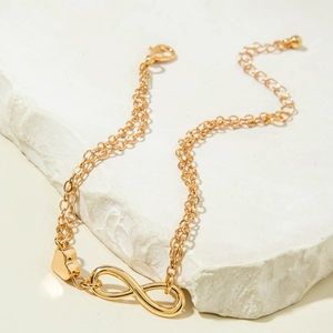 Detail of a gold double-layer infinity and heart charm anklet on a white stone