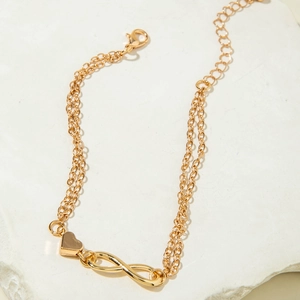 Detail of gold double-layered anklet with infinity symbol and heart charm on stone