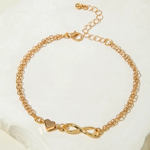 Detail of gold double-layer anklet with heart and infinity charms on stone background