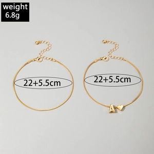 Detail of layered gold rhinestone anklets with letter A pendant and heart charm