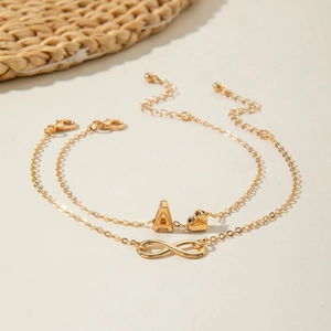 Close-up of gold layered anklets with alphabet A, heart, and infinity symbol charms