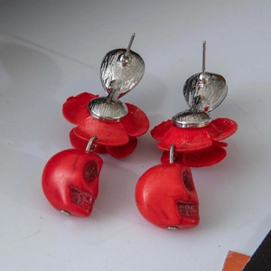 Détail de boucles d'oreilles tête de mort rouge avec pétales et clous argentés Halloween