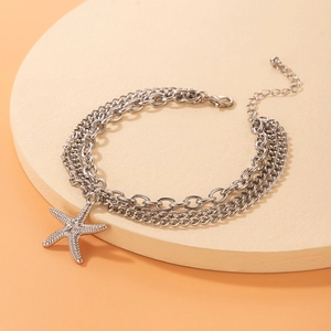 Close-up of a silver triple-layered chain anklet featuring a textured starfish pendant