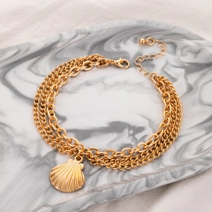 Close-up of golden multi-layer anklet with seashell pendant on marble tray