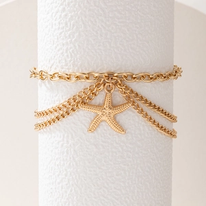 Close-up of gold multi-layer anklet featuring a textured starfish charm on white pedestal